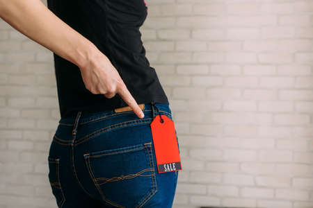 Woman tries on clothes and points to the Black Friday tag. Back view of a slender female butts in blue jeans. Shopping concept, seasonal discounts. Advertising sign.の写真素材
