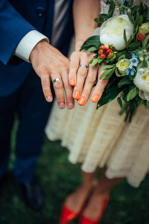 Focus on the hands of bride and groom, wedding bouquet, top view, blurred background. Platinum or silver rings on the fingers of newlyweds, close-up.の写真素材