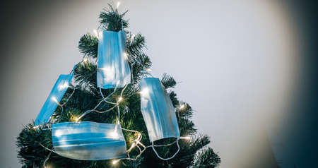 Symbol of the new coming year 2021. Medical masks hanging on the Christmas tree in the light of garlands. Holidays during quarantine due to covid 19.の写真素材