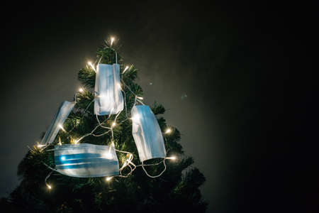 Close-up of Christmas tree lit with garlands, decorated with protective medical masks in a dark room.の写真素材