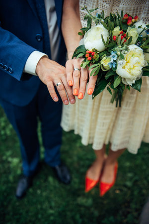 Focus on the hands of bride and groom, wedding bouquet, top view, blurred background. Platinum or silver rings on the fingers of newlyweds, close-up.の写真素材