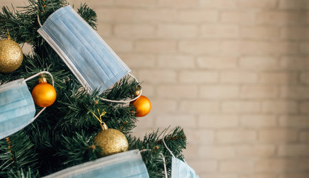 Christmas tree decorated with blue medical masks and golden balls, close up. Concept of 2021 new year amid the coronavirus pandemic. Symbol of holiday in quarantine. Image with space for text.の写真素材