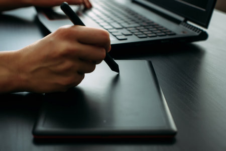 Female designer illustrator working with graphic tablet in modern office. Side view creative artist's hands drawing on digital tablet with pen, close up, black background.の写真素材