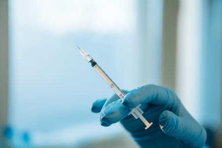 Thin syringe for injection in the doctor's hand, close-up, light background. Hand in medical glove...