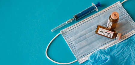 Coronavirus vaccine in bottles on blue background with copy space. Vials of medicine for covid19, syringe, medical face mask and gloves, top view. Immunization concept banner.の写真素材