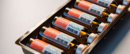 Coronavirus vaccine in box, close-up. Vials of medicine for covid19 lie in a row, white background. Focus on label with inscription.の写真素材