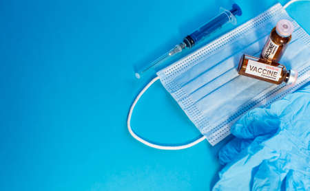 Coronavirus vaccine in bottles on blue background with copy space. Vials of medicine for covid19, syringe, medical face mask and gloves, top view.の写真素材