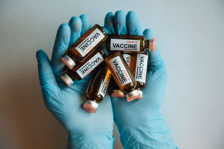 Blue gloved hands holding glass vials containing coronavirus covid-19 vaccine, top view. Ampules of covid vaccine close up. Concept of mass immunization.の写真素材