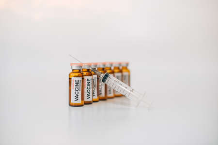 Dark glass vaccine phials with label and medical syringe with needle up, on white background with copy space. Image for advertising of pharmaceutical products, selective focus.の写真素材