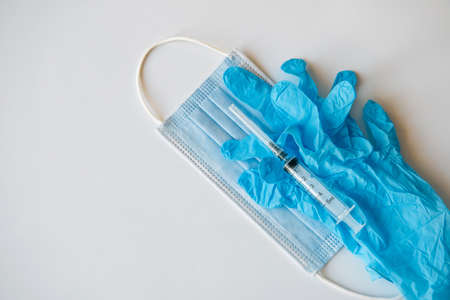 Medical mask, syringe, blue latex gloves on white background with copy space, close-up. Concept of vaccination of the population.の写真素材