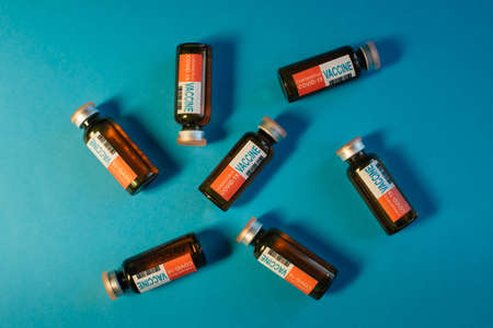 Dark glass vials of coronavirus vaccines lie randomly on blue background, close-up. Covid-19 concept. Completion of development of antiviral drug, mass vaccination of population.の写真素材