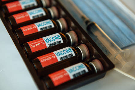 Coronavirus vaccine in box, close-up. Vials of medicine for covid19, syringe, medical face mask....