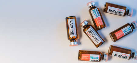 Vials of different coronavirus vaccine lie randomly on white background, close-up. Covid-19 banner with copy space. Completion of development of antiviral drug, mass vaccination of population.の写真素材