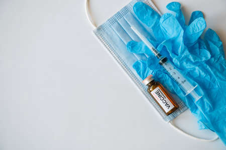 Coronavirus COVID 19 vaccine vial and syringe on medical face mask and blue gloves, white background, copy space. World vaccination concept.の写真素材