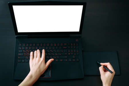 Cropped shot of graphic designer's hands working on graphic tablet and laptop with blank screen on black office table. Freelance, Illustrator. Creativity, remote work, outsourcing.の写真素材