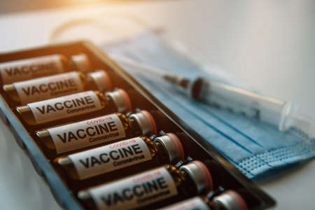 Close-up of glass vials with Covid-19 vaccine, medical mask, syringe. Scientific developments in the fight against viral infection, coronavirus, pulmonary pneumonia.の写真素材