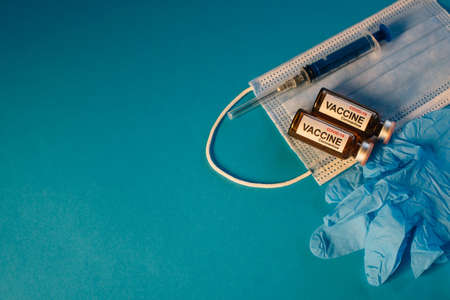 Coronavirus vaccine in bottles on blue background with copy space. Vials of medicine for covid19, syringe, medical face mask and gloves, top view.の写真素材