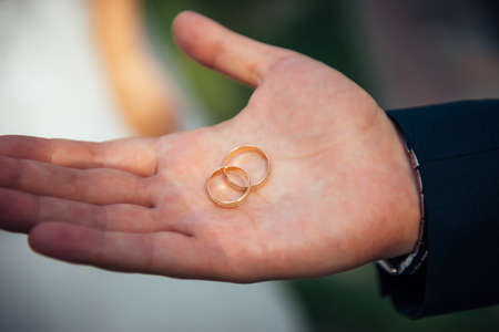 Two gold wedding rings lie on a man's open palm, close-up. Young groom holding wedding rings in his...