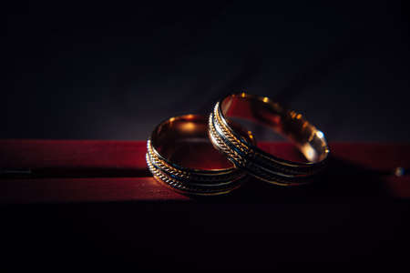 Two vintage wedding rings on dark red background, close-up. Gold rings with a pattern, selective focus. Jewelry for the bride and groom.の写真素材