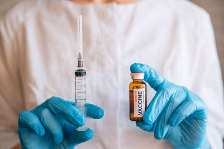 Scientist or doctor's hands holding syringe and coronavirus vaccine vial, close up. Concept of covid immunization, clinical trials of new medicine on human.の写真素材