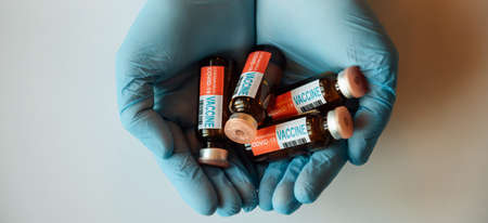 Blue gloved hands holding glass vials containing coronavirus covid-19 vaccine, top view. Ampules of covid vaccine close up. Concept of mass immunization.の写真素材