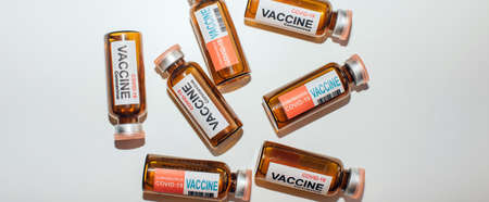 Vials of different coronavirus vaccine lie randomly on white background, close-up. Covid-19 banner with copy space. Completion of development of antiviral drug, mass vaccination of population.の写真素材