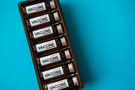Bottles of vaccine to fight the coronavirus pandemic. Victory over Sars-cov-2 / COVID-19. Some ampoules with vaccine in a box on blue background with copy space.の写真素材