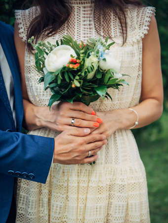 Hands of the bride and groom with wedding rings, bouquet of fresh flowers, vintage lace dress. Concept of marriage, love, family life.の写真素材