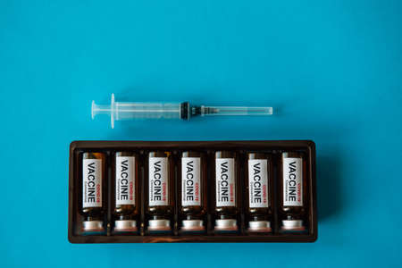 Box of ampoules with label and syringe on blue background with copy space, close-up. Coronavirus...