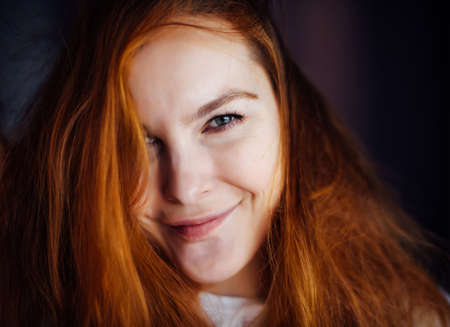 Portrait of beautiful young woman with thick, tousled red hair, close-up. Gray-eyed beauty looking...