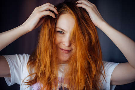 Portrait of beautiful adult young woman with red tousled hair, close-up, blurred background. Sexy brunette touches her long hair and looks at camera.の写真素材