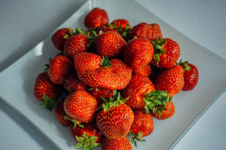 Fresh ripe strawberries on glass plate, top view, close-up. Beautiful red berries with green leaves. Organic food from home greenhouse for healthy diet.の写真素材