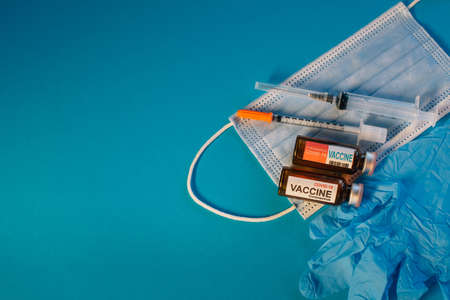 Coronavirus vaccine in bottles on blue background with copy space. Vials of medicine for covid19, syringe, medical face mask and gloves, top view.の写真素材