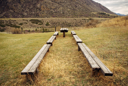 Wooden benches and old table made of pine boards in a clearing against the mountains. Abstract image. Place for tourist camp.の写真素材