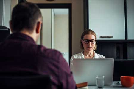 Adult young married couple sitting at a table in the kitchen, remotely working together on laptops,...