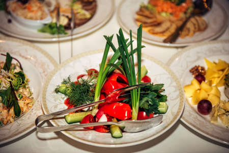Portioned salad of fresh vegetables and herbs on plate, close-up. Coarsely chopped cucumbers, tomatoes, bell peppers, radishes. Banquet at restaurant.の写真素材