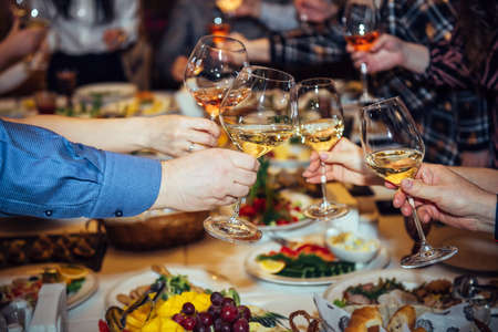 Toast at the festive table. Hands holding glasses with alcoholic beverages, close-up. Relatives and friends clinking wineglasses.の写真素材