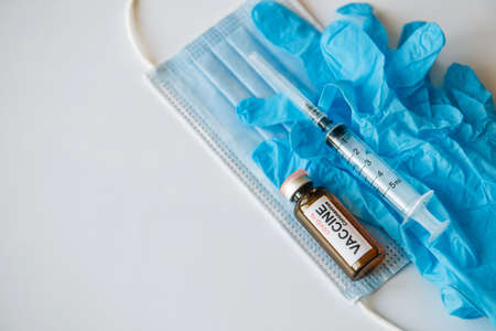 vaccine vial and syringe on medical face mask and blue gloves, white background, copy space. World vaccination concept.の写真素材