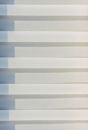 Abstract geometric horizontal lines white and gray gradient color. Repeating pattern, background texture, design of striped lines. Roller blinds illuminated by the sun, close-up.の写真素材