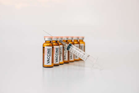 Dark glass vaccine phials with label and medical syringe with needle up, on white background with copy space. Image for advertising of pharmaceutical products, selective focus.の写真素材