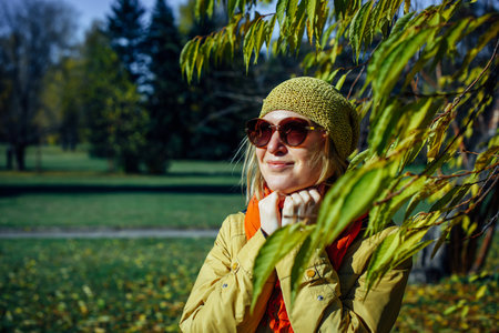 Portrait of attractive girl in sunglasses and red scarf on the background of yellow foliage in autumn park. Young woman enjoying walk on fall sunny day.の写真素材