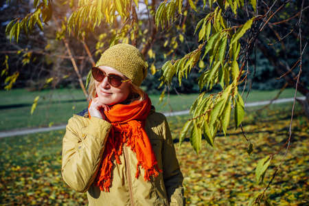 Portrait of attractive girl in sunglasses and red scarf on the background of yellow foliage in autumn park. Young woman enjoying walk on fall sunny day.の写真素材