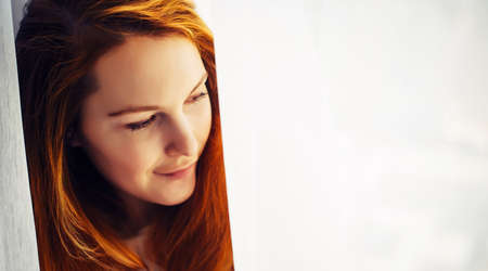 Gorgeous young redhead girl with long hair, close-up, copy space. Portrait of beautiful smiling woman with perfect skin on light blurry background.の写真素材