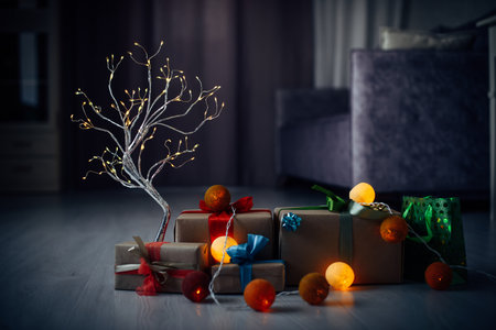 Christmas background with silver garland, burning colorful balls. Gift boxes decorated with ribbons and bows on the floor in cozy home interior. New year eve.の写真素材