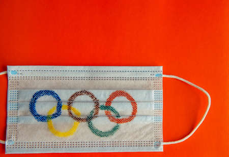 Novosibirsk, Russia - 06.01.2022. Olympic rings painted on medical mask, red chinese background. Concept of virus security during the Olympic games 2022. Copy space.のeditorial素材