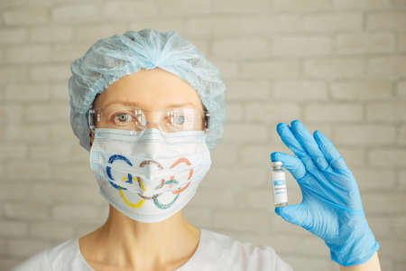 Female doctor in medical mask and cap holding coronavirus vaccine in her hand. Mandatory vaccination of participants of the 2022 Olympics. Novosibirsk, Russia - 06.01.2022.のeditorial素材