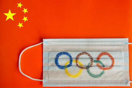 Novosibirsk, Russia - 06.01.2022. Olympic rings painted on medical mask on the background of Chinese red flag. Concept of Olympic Games in Beijing 2022.のeditorial素材