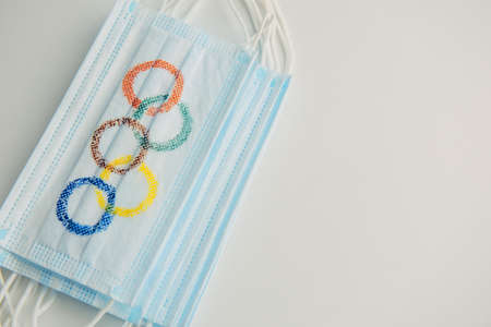 Concept of coronavirus security during 2022 Olympic Games. Olympic rings painted on medical masks lying in a pile on a white background. copyspace. Novosibirsk, Russia - 06.01.2022.のeditorial素材