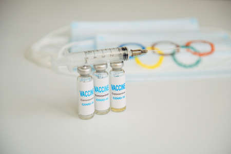 Novosibirsk, Russia - 06.01.2022. Medical masks with Olympic rings, vials with coronavirus vaccine on white background. Concept of virus security at the 2022 Olympics in Beijing.のeditorial素材