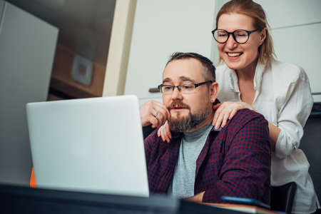 Bearded man and woman with eyeglasses using laptop in the home interior, communicate with friends online, laugh and grimace.の写真素材
